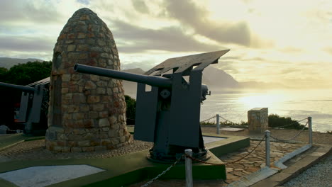 Hermanus-Amanecer-Dorado-Sobre-Walker-Bay-Con-Vista-Al-Histórico-Monumento-A-Los-Caídos-En-La-Guerra-Con-Un-Mojón-De-Piedra-Y-Dos-Cañones-Navales