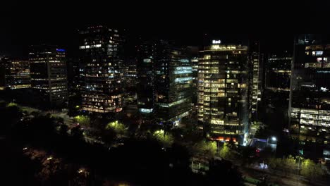 Paisaje-Urbano-Nocturno-De-La-Capital-Chilena-De-Santiago-Por-La-Noche-En-El-Barrio-Moderno-De-Nueva-Las-Condes,-Iluminación-De-Edificios-Altos,-Establecimiento-De-Tomas-Panorámicas-De-La-Ciudad