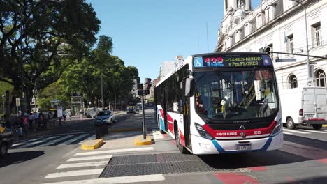 Bus-Autobus-drive-Buenos-Aires-city-public-transport-traffic-at-Rivadavia-avenue-urban-scene-in-argentinian-capital-asphalted-road-with-public-green-park-and-skyline-in-autumn