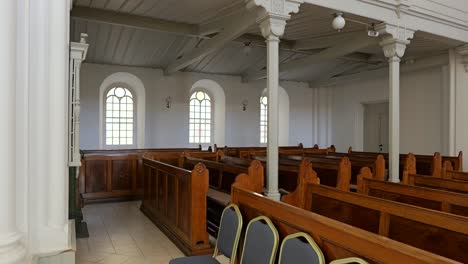Tracking-view-along-front-of-Lutheran-church-sanctuary,-rows-of-old-wooden-pews