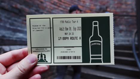 Hand-holding-Jameson-Distillery-tour-ticket-in-foreground-while-walking-up-stairs