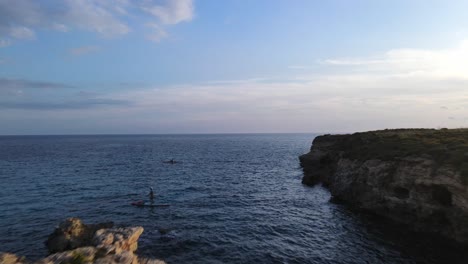 Stand-Up-Paddle-Boarder-Umrundet-Felsen-Am-Strand-Von-Binigaus-Auf-Menorca-Bei-Sonnenuntergang