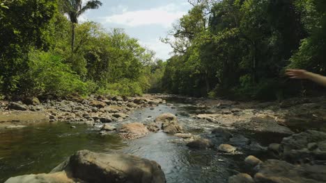 Drohnenflug-Durch-üppigen-Dschungelfluss-Mit-Sportlichem-Weiblichen-Model,-Das-Mit-Erhobenen-Armen-Posiert,-4K-Costa-Rica