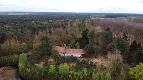 Aerial-rotating-shot-above-abandoned-mansion-in-the-middle-of-the-forest-with-agricultural-fields-in-the-background