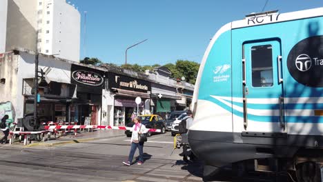 Local-people-walk-next-to-sarmiento-train-railway-public-transport-of-buenos-aires-city-argentina,-pedestrians-travel-to-work-on-a-sunny-day,-flores-station