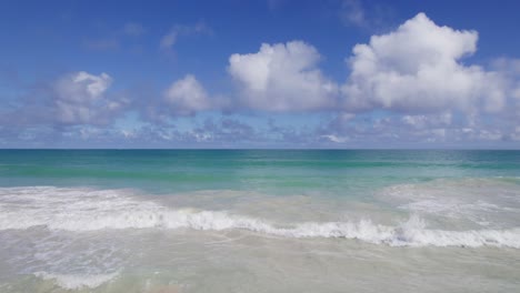 Drohnenaufnahmen-Beginnend-An-Einem-Weißen-Sandstrand-über-Dem-Türkisfarbenen-Wasser-Der-Waimanalo-Bucht-Mit-Strahlend-Blauem-Himmel-Und-Bauschigen-Weißen-Wolken