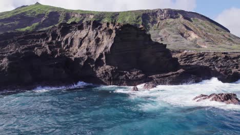 aerial-footage-of-the-coastline-of-Oahu-Hawaii-with-turquoise-water-of-the-Pacific-Ocean-and-white-capped-waves-crashing-the-shore-line-of-the-volcanic-formations-and-lush-mountains-in-the-background