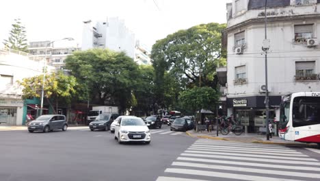 Autos-Fahren-Und-Biegen-Auf-Der-Überholspur-Der-Avenue-Directorio-In-Der-Stadt-Buenos-Aires-Ab,-Im-Herbst-Wartet-Ein-Argentinischer-Bus-Mit-öffentlichen-Verkehrsmitteln-An-Einer-Haltestelle-Mit-Ampel-Und-Panoramablick-Auf-Die-Stadt