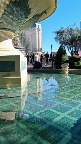 Vertical-Video-Las-Vegas-USA,-People-in-Front-of-Bellagio-Fountain-With-View-of-Eiffel-Tower-and-Paris-Casino-Hotel-on-Sunny-Day