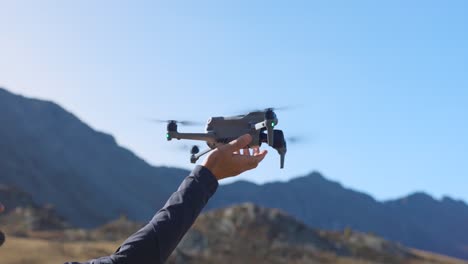 Drone-Desciende-En-Mano-Del-Piloto-Con-Montañas-En-El-Fondo