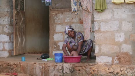 Tanzania-mother-bathing-young-baby-in-basin-on-the-floor-outside-house-on-the-porch