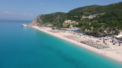 La-Playa-De-Kathisma-En-La-Isla-De-Lefkada-Ofrece-A-Los-Visitantes-Una-Playa-De-Arena-Con-Sombrillas-Y-Suaves-Olas-Del-Océano-Color-Turquesa.