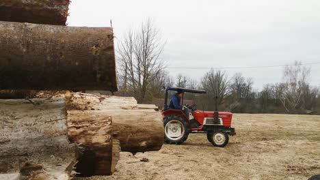 Worker-in-sawmill-driving-red-yanmar-m1610d-tractor-pulling-a-stack-of-planks