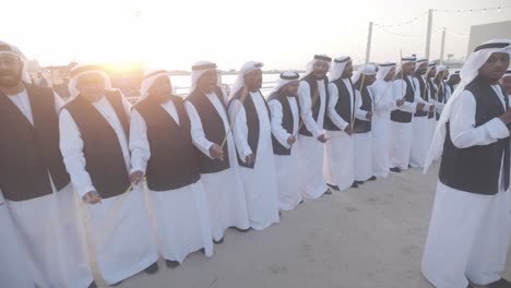 Danza-Tradicional-De-Los-Emiratos-Árabes-Unidos-Con-El-Palo-En-Grupo-Mientras-Canta-Durante-Una-Puesta-De-Sol-épica