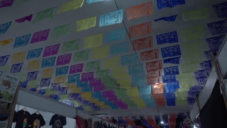 Mexican-papel-picado-decorations-hanging-overhead-for-Day-of-the-Dead-adorning-a-bazaar-in-Oaxaca,-Mexico