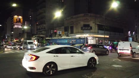 Agentes-De-Policía-En-Motocicletas-Con-Luces-Azules-Por-La-Noche-En-El-Tráfico-De-Buenos-Aires-En-La-Vibrante-Ciudad-Latina,-Policía-Controlando-El-Tránsito-En-La-Avenida-Rivadavia,-Durante-La-Noche,-Tiendas-Comerciales-Alrededor