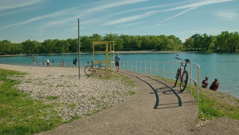 Capture-La-Vibrante-Atmósfera-Del-Lago-Jarun-De-Zagreb-En-Un-Día-Soleado,-Con-Bicicletas-Estacionadas-Y-Gente-Disfrutando-Del-Tranquilo-Entorno-Junto-Al-Lago-En-Este-Metraje-Estable.