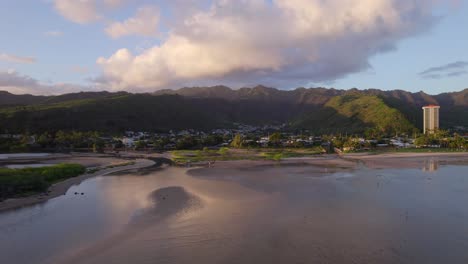 drone-footage-of-East-Honolulu-Hawaii-from-the-water-view-of-mamala-bay-with-the-pink-glow-from-the-setting-sun-reflecting-off-the-water-and-white-puffy-clouds