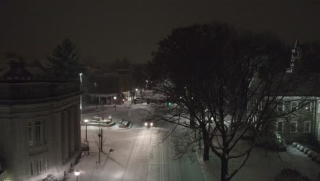 Toma-Aérea-Sobre-Una-Carretera-Nevada-En-El-Centro-De-Lititz-Por-La-Noche-Mirando-Hacia-La-Plaza