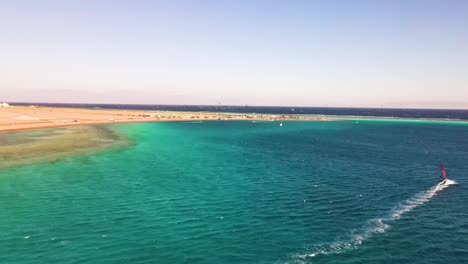 Windsurfer-over-the-tranquil-turquoise-waters-of-Dahab,-Egypt,-where-the-exhilarating-harmony-of-wind-and-waves-meets-the-serenity-of-coastal-beauty,-the-spirit-of-aquatic-adventure-and-leisure