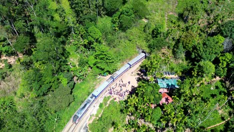Aerial-drone-scenic-view-of-train-with-locomotive-carriages-travelling-along-railway-line-entering-into-tunnel-with-people-standing-near-Ella-Sri-Lanka-Asia
