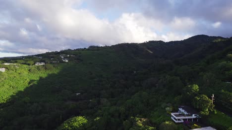 Toma-Aérea-Sobre-Un-Exuberante-Barranco-De-Montaña-Sombreado-De-Verde-Salpicado-De-Edificios-En-La-Isla-De-Oahu-En-Las-Islas-Hawaianas.