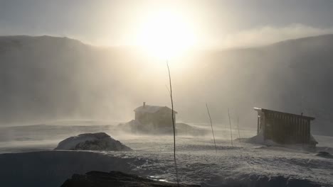 Snow-blows-around-two-small-mountain-cabins-at-sunset,-Voss,-Norway