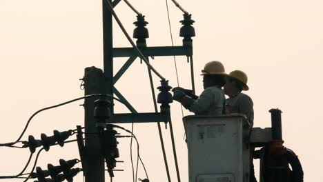 Ingenieros-Eléctricos-Enrollando-Cinta-Resistente-Alrededor-De-Un-Aislante-De-Un-Poste-Eléctrico-Para-Solucionar-El-Problema-De-Electricidad-En-Un-Barrio-De-La-Ciudad-De-Bangkok,-En-Tailandia.