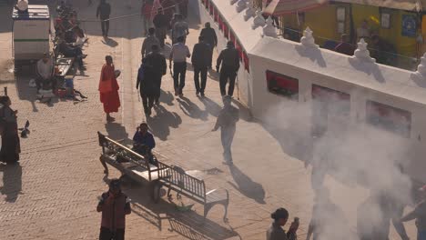 Toma-Elevada-Retroiluminada-De-Gente-Caminando-Por-La-Sección-Exterior-Del-Templo-Boudhanath,-Katmandú,-Nepal