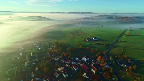 Vista-Aérea-De-La-Brumosa-Mañana-De-Otoño-Sobre-El-Pueblo-Y-El-Paisaje-Verde-De-La-Campiña-Alemana,-Disparo-De-Drones