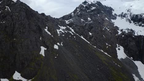 Slow-motion-ascent-looking-over-snowy-high-altitude-mountain-peak-in-Fiordland,-New-Zealand,-South-Island