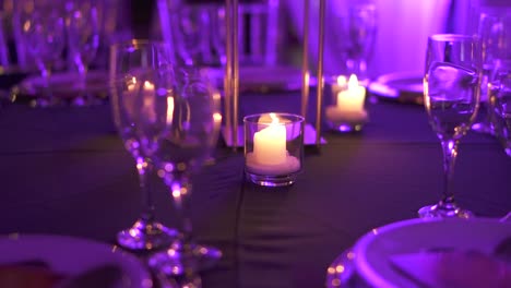 Mesa-De-Banquete-Con-Vajilla-De-Cristal-Y-Velas-En-Una-Habitación-Con-Iluminación-Violeta