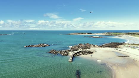 Circling-aerial-shot-of-boat-on-sandy-bottom-of-old-harbour-in-Guernsey-Channel-Islands-on-bright-sunny-day-with-clear-calm-water-rocks-and-golden-sand