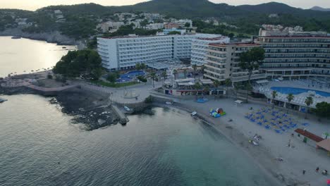 aerial-dolly-over-oceanfront-hotel-buildings-at-sunset,-in-hotel-zone,-surrounded-by-tropical-jungle