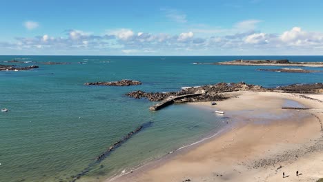 Enthüllung-Des-Bootes-Auf-Dem-Sandboden-Des-Alten-Hafens-Auf-Den-Kanalinseln-Von-Guernsey-An-Einem-Hellen,-Sonnigen-Tag-Mit-Klarem,-Ruhigem-Wasser,-Felsen-Und-Goldenem-Sand