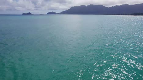 Imágenes-De-Drones-A-Través-De-Aguas-Turquesas-Hacia-Una-Montaña-Recortada-En-El-Horizonte-En-La-Bahía-De-Waimanalo-Oahu-Hawaii