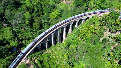 Aerial-drone-scenic-view-of-train-on-tracks-crossing-over-Ella-Nine-Arch-Bridge-surrounded-by-farming-forest-colonial-landmark-Sri-Lanka-Asia-travel-tourism