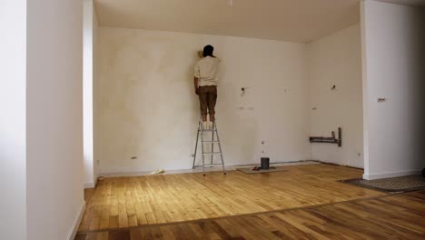 Hombre-Trabajador-En-La-Escalera-Aplicando-Pintura-De-Cal-En-La-Pared-Interior-De-La-Casa