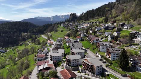 Pintoresca-Ciudad-Suiza-Con-Apartamentos-De-Hotel-En-Una-Colina-Con-Pastos-Verdes-Y-Montañas-Nevadas-Al-Fondo