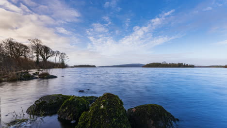 Time-lapse-of-a-rocky-shore-foreground-with-forest-in-distance-on-a-cloudy-sunny-day-at-Lough-Key-in-county-Roscommon-in-Ireland