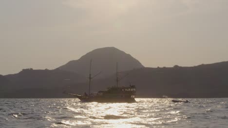 Eine-Yacht-Kreuzt-In-Den-Gewässern-Nahe-Der-Insel-Komodo,-Vor-Der-Kulisse-Einer-Kleinen,-Bergigen-Insel