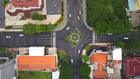 El-Bullicioso-Tráfico-Fluye-En-El-Cruce-De-Surabaya,-Flanqueado-Por-Antiguos-Edificios-De-Estilo-Colonial-Y-Espacios-Verdes-Junto-A-Peatones.