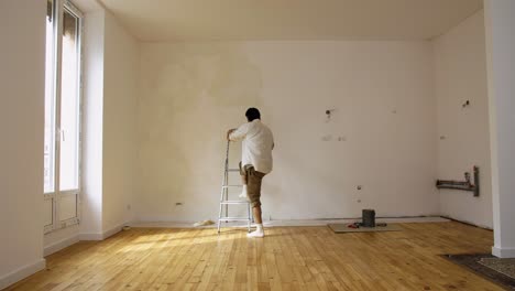 Man-Working-In-House,-Applying-Limewash-Paint-On-Wall-With-Paintbrush