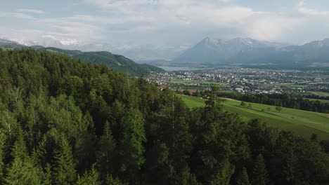 Aerial-of-a-forest-with-a-small-town-and-mountains-in-the-background