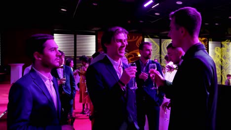 three-well-dressed-friends-in-suits-at-a-student-gala-toasting-together-with-their-glass-of-champagne,-pink-lighting-dimmed