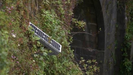 Pequeño-Panel-Solar-Fotovoltaico-Instalado-En-Una-Antigua-Pared-Llena-De-Plantas.