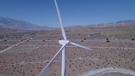 Drone-focuses-on-one-working-windmill-in-the-desert,-with-numerous-windmills-visible-in-the-far-background