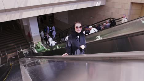 Mujer-Musulmana-Con-Gafas-Saboreando-El-Paseo-En-Una-Escalera-Mecánica-En-Un-Centro-Comercial