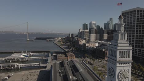 Drone-circles-San-Francisco-Ferry-Building-clock-tower-closely-on-clear-day,-revealing-180-degree-downtown-view-from-Embarcadero