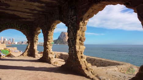 Dramatische-FPV-Drohnenansicht-Von-Calpe,-Spaniens-Berühmtem-Berg-Und-Küstenabschnitt-Peñon-D&#39;Ifach---Auch-Bekannt-Als-Calpe-Felsen:-Durch-Mit-Graffiti-Besprühte-Runde-Fenster-In-Einem-Verlassenen-Graffiti-Gebäude